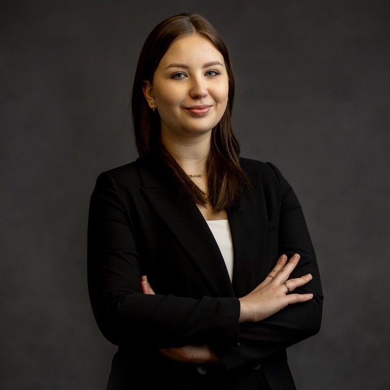 Confident woman in a black blazer with arms crossed against a dark background.